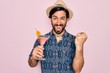 Young handsome hispanic bohemian hipster man with bear drinking a summer cocktail screaming proud and celebrating victory and success very excited, cheering emotion