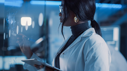 Aufkleber - In the Research Laboratory Smart and Beautiful African American Female Scientist Wearing White Coat and Protective Glasses Writes Formula on Glass Whiteboard, References Her Tablet Computer