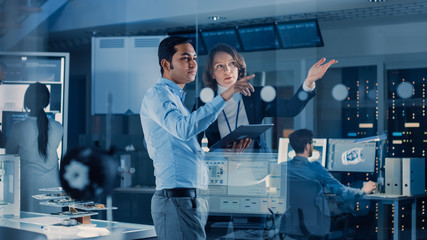 Wall Mural - In Technology Research Facility: Female Project Manager Talks With Chief Engineer, they Consult Tablet Computer. Team of Industrial Engineers, Developers Work on Engine Design Using Computers