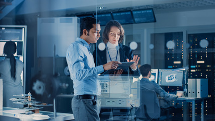 Poster - In Technology Research Facility: Female Project Manager Talks With Chief Engineer, they Consult Tablet Computer. Team of Industrial Engineers, Developers Work on Engine Design Using Computers