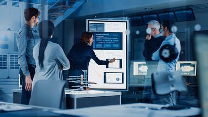 Poster - Engineers Meeting in Research Laboratory: Female Engineer Leads Presentation Writes on Interactive Digital Whiteboard, Shows Blueprint, Data Analytics and Neural Network while Colleagues Listening