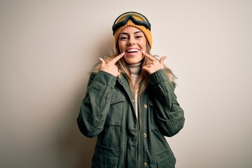 Sticker - Young brunette skier woman wearing snow clothes and ski goggles over white background Smiling with open mouth, fingers pointing and forcing cheerful smile