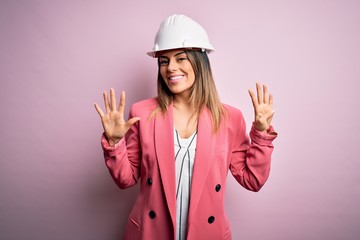 Poster - Young beautiful brunette architect woman wearing safety helmet over pink background showing and pointing up with fingers number nine while smiling confident and happy.