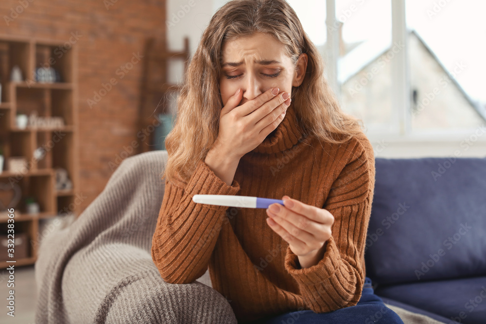 Sad young woman with pregnancy test at home