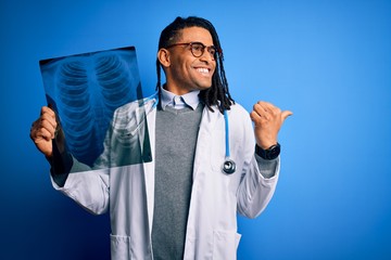 Young african american afro doctor man with dreadlocks holding chest lung xray pointing and showing with thumb up to the side with happy face smiling