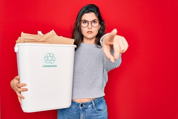 Sticker - Young beautiful woman holding recycle cardboard containter recycling for eco environment pointing with finger to the camera and to you, hand sign, positive and confident gesture from the front