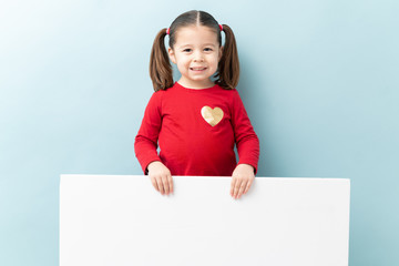 Wall Mural - Portrait of a pretty little Caucasian girl holding a big white sign and smiling in a studio