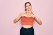 © Krakenimages.com - Young beautiful fitness woman wearing sport excersie clothes over pink background smiling in love showing heart symbol and shape with hands. Romantic concept.