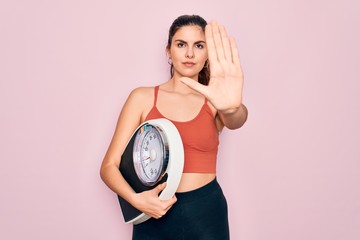 Sticker - Young beautiful fitness woman wearing sport clothes holding weighting machine scale with open hand doing stop sign with serious and confident expression, defense gesture