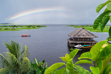View Of The Amazon River Tributary In Iquitos, Peru. A Rainbow Over The River And A Beautiful Building Floating On The Water.