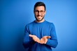 © Krakenimages.com - Young handsome man with beard wearing casual sweater and glasses over blue background Smiling with hands palms together receiving or giving gesture. Hold and protection