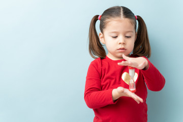 Wall Mural - Serious looking little girl looking at a sand timer while practicing self-control during timeout in a studio with copy space