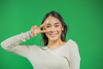 Close-up portrait of a nice cheerful happy positive cute adorable attractive charming glamorous gorgeous black hair lady of Asian appearance shows a v-mark near the eye isolated over green background