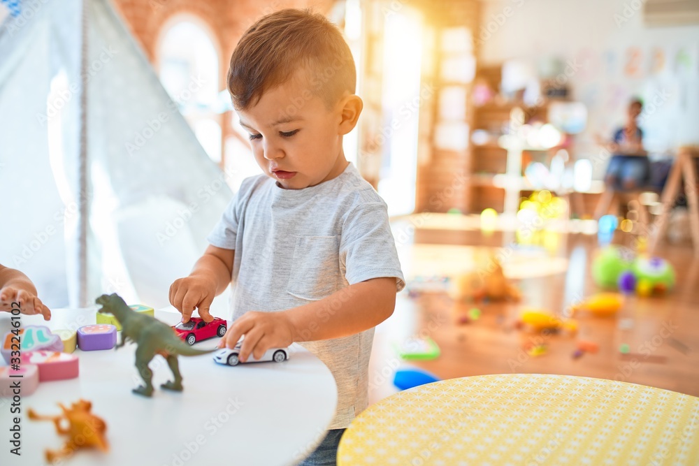 Adorable toddler smiling happy. Standing playing around lots of toys at kindergarten