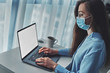 © Goffkein - Business woman in glasses and a medical protective mask online working from home at the laptop during self isolation and quarantine. Coronavirus outbreak, flu epidemic and covid ncov novel