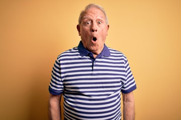 Poster - Grey haired senior man wearing casual navy striped t-shirt standing over yellow background afraid and shocked with surprise expression, fear and excited face.