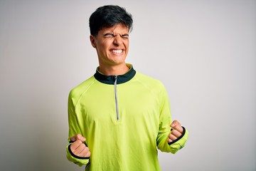 Canvas Print - Young handsome sportsman doing sport wearing sportswear over isolated white background very happy and excited doing winner gesture with arms raised, smiling and screaming for success. Celebration