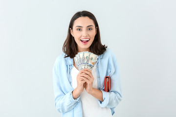 Wall Mural - Young woman with wallet and money on light background