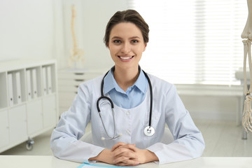 Wall Mural - Female orthopedist at table near human skeleton model in office