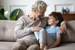 © fizkes - Happy loving mature grandfather sit rest on sofa in living room enjoy weekend with little grandchild, smiling senior grandparent relax on couch at home talk chat with cute small preschooler grandson