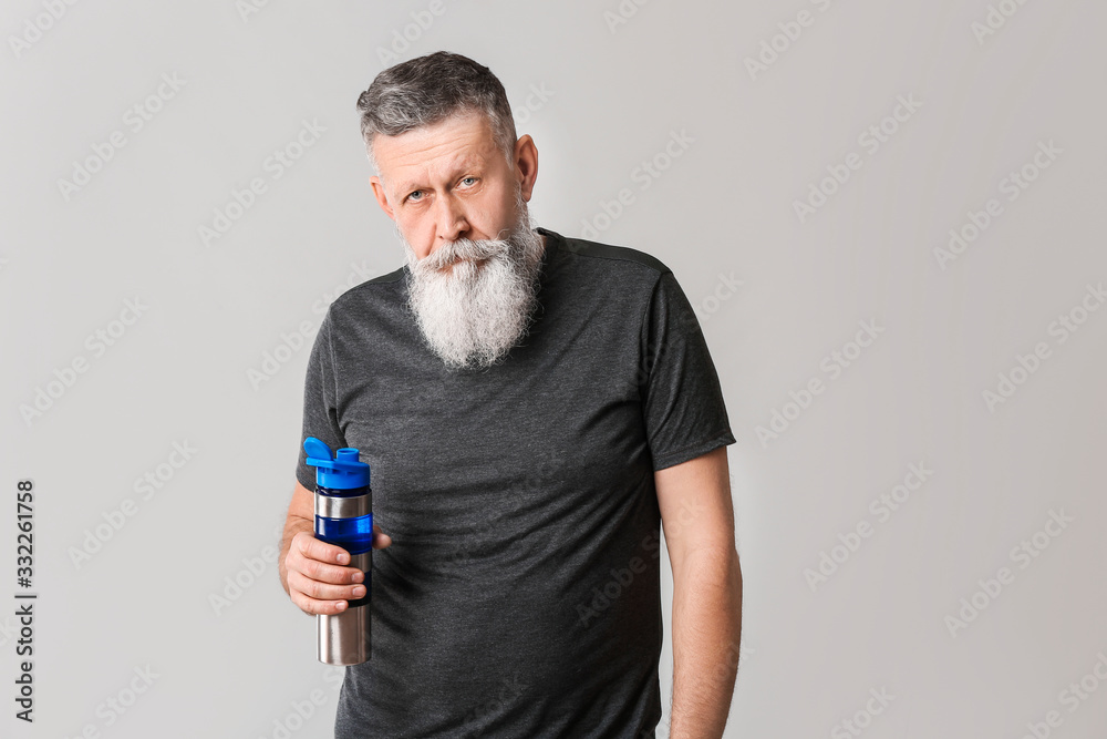 Sporty elderly man with bottle of water on grey background