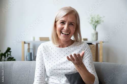 Cuadros en Lienzo Happy mature blonde lady sitting on couch, holding video call with friends, head shot close up portrait