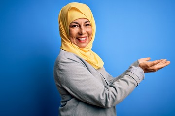 Wall Mural - Middle age brunette business woman wearing muslim traditional hijab over blue background pointing aside with hands open palms showing copy space, presenting advertisement smiling excited happy