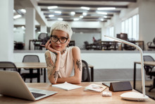 Creative Job. Pretty And Young Tattooed Business Lady In Eyewear Looking At Camera While Working Alone In The Modern Office