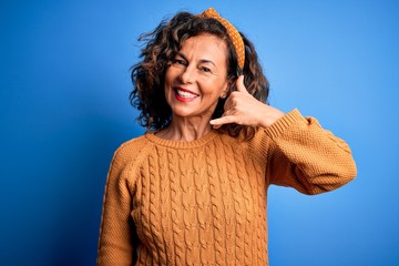 Middle age beautiful woman wearing casual yellow sweater over isolated yellow background smiling doing phone gesture with hand and fingers like talking on the telephone. Communicating concepts.