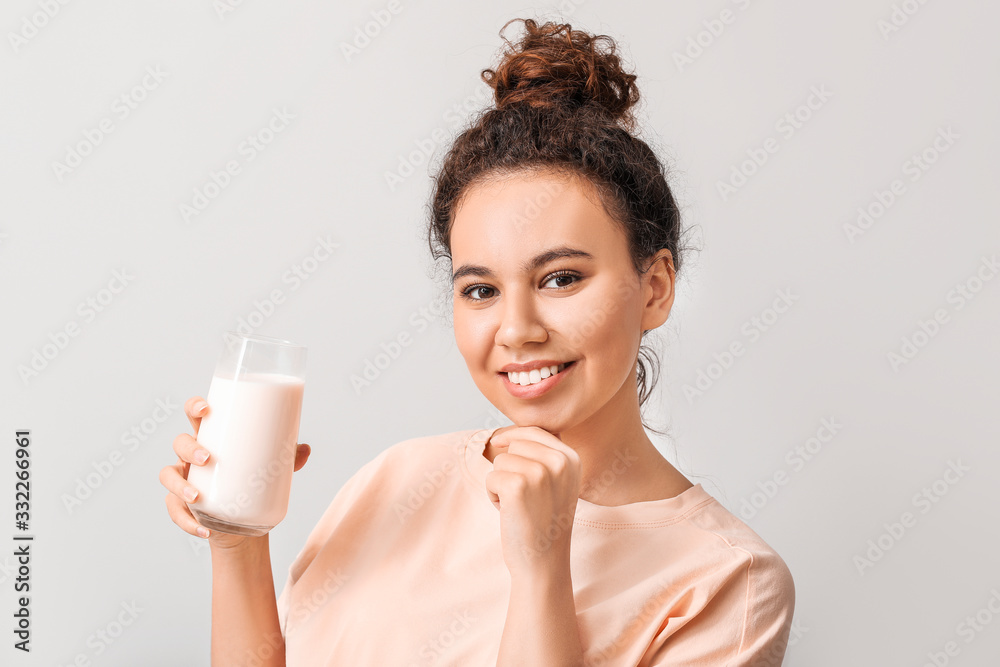 Young African-American woman with milk on light background