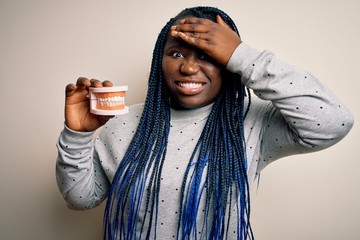 Poster - African american plus size woman with braids holding plastic teeth over white background stressed with hand on head, shocked with shame and surprise face, angry and frustrated. Fear and upset