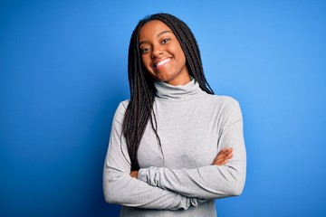 Sticker - Young african american woman standing wearing casual turtleneck over blue isolated background happy face smiling with crossed arms looking at the camera. Positive person.