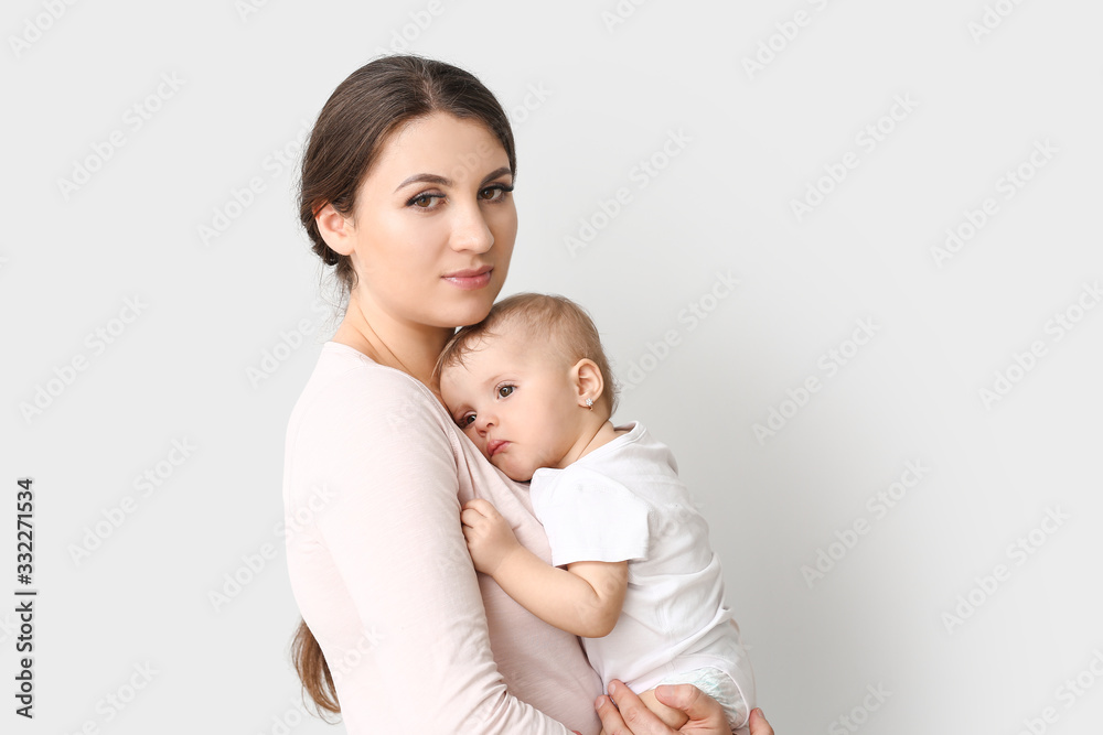 Happy mother with cute little baby on light background