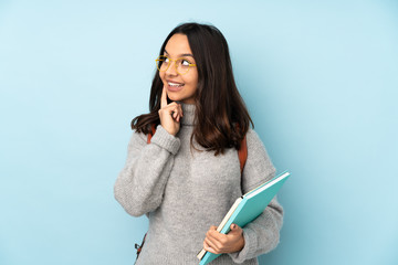 Young mixed race woman going to school isolated on blue background thinking an idea while looking up