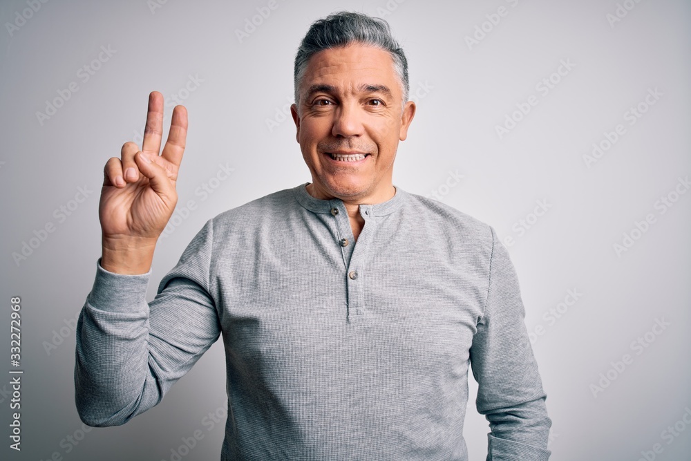 Middle age handsome grey-haired man wearing casual t-shirt over white background smiling with happy face winking at the camera doing victory sign. Number two.