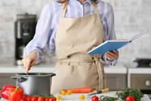 Woman With Cook Book Preparing Food In Kitchen