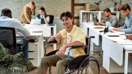 Working independently, together. Guy in a wheelchair working in the office