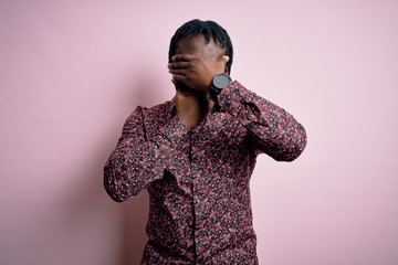 Poster - Young handsome african american man wearing casual shirt standing over pink background Covering eyes and mouth with hands, surprised and shocked. Hiding emotion