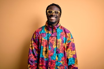 Poster - Handsome african american man wearing colorful coat and glasses over yellow background with a happy and cool smile on face. Lucky person.