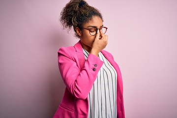 Poster - Beautiful african american businesswoman wearing jacket and glasses over pink background tired rubbing nose and eyes feeling fatigue and headache. Stress and frustration concept.