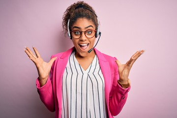 Canvas Print - Young african american call center agent girl wearing glasses working using headset celebrating crazy and amazed for success with arms raised and open eyes screaming excited. Winner concept