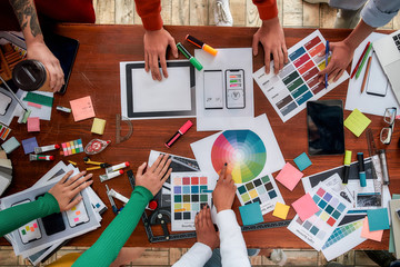 Wall Mural - mobile app design. top view of designers discussing sketches, choosing colors from palettes lying on