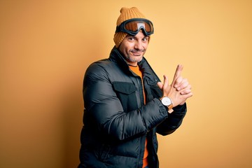 Young handsome skier man skiing wearing snow sportswear using ski goggles Holding symbolic gun with hand gesture, playing killing shooting weapons, angry face