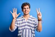 © Krakenimages.com - Young blond handsome man with curly hair wearing casual striped sweatshirt showing and pointing up with fingers number seven while smiling confident and happy.