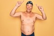 © Krakenimages.com - Middle age senior grey-haired swimmer man wearing swimsuit, cap and goggles smiling amazed and surprised and pointing up with fingers and raised arms.