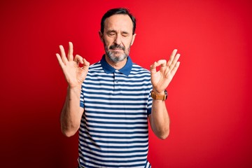 Middle age hoary man wearing casual striped polo standing over isolated red background relax and smiling with eyes closed doing meditation gesture with fingers. Yoga concept.