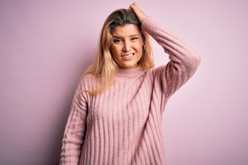 Poster - Young beautiful blonde woman wearing casual pink sweater over isolated background confuse and wonder about question. Uncertain with doubt, thinking with hand on head. Pensive concept.