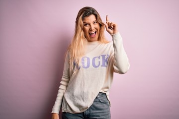 Poster - Young beautiful blonde woman wearing casual sweater standing over pink background pointing finger up with successful idea. Exited and happy. Number one.