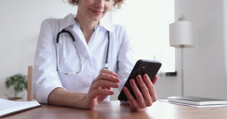 Wall Mural - Female doctor wearing white coat holding cell using smart phone apps texting message to remote patient. Practice of medicine and public health care supported by mobile devices concept. Close up view