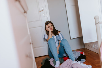  A teenage caucasian girl is sitting next to a closet in her room